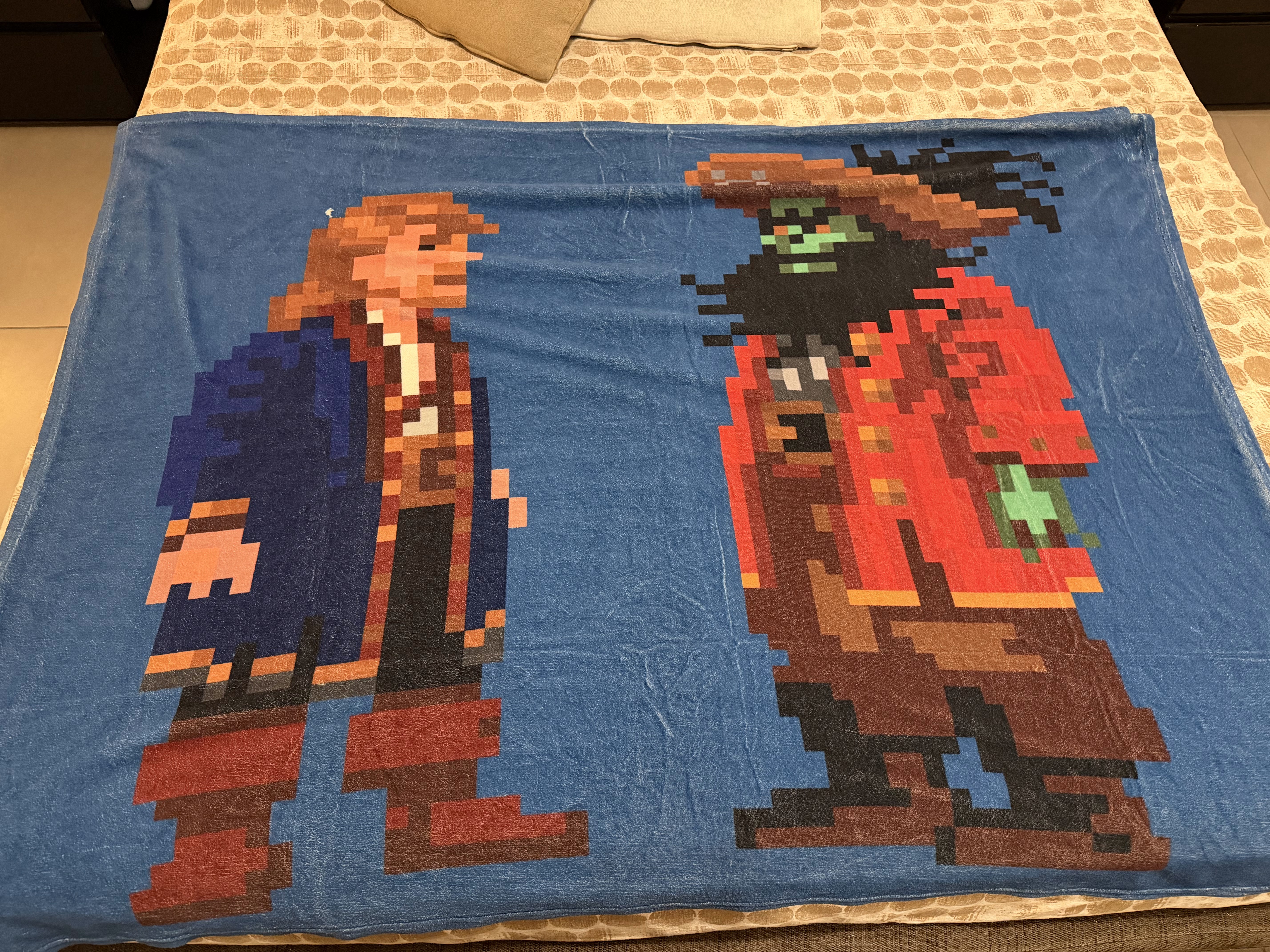 Una coperta blu con Guybrush e LeChuck in pixel art, distesa sul letto.