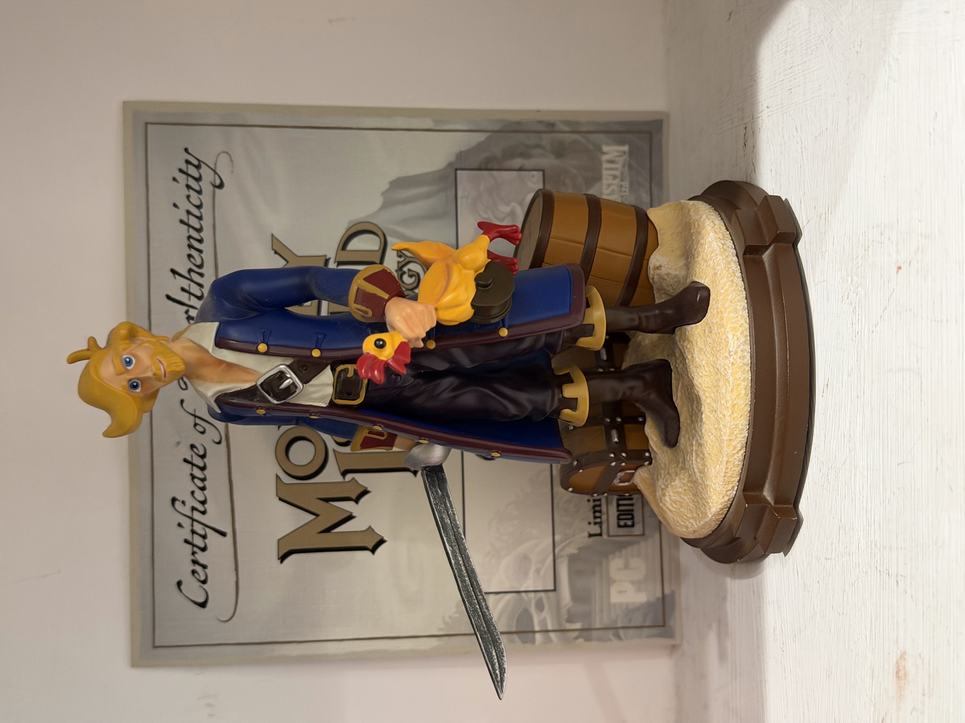 Una statuetta di Guybrush con spada e pollo di gomma, davanti al certificato della collezione.