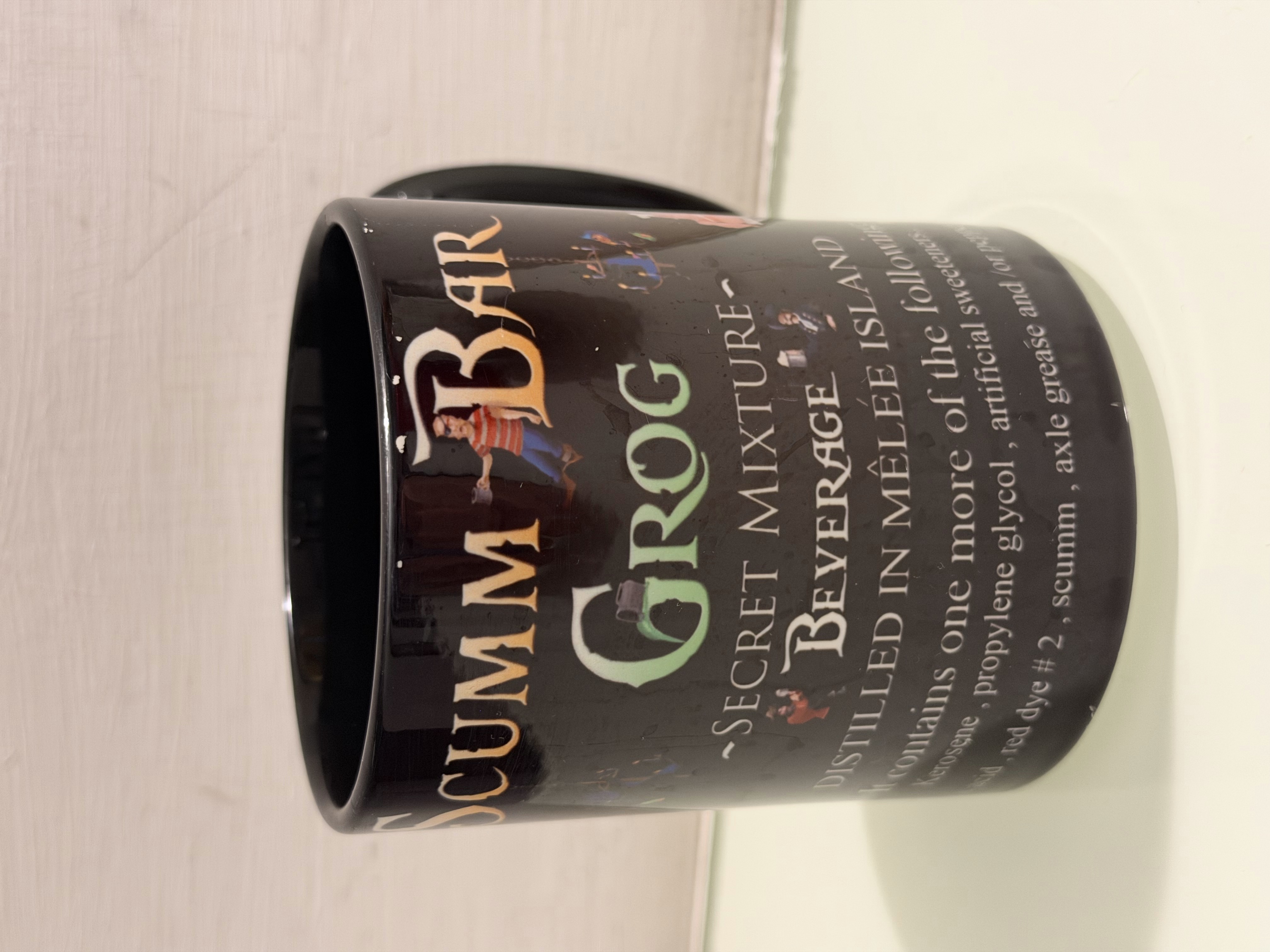 Una tazza nera decorata con la scritta Scumm Bar Grog e personaggi della saga.